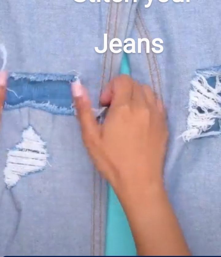 Hands stitching a rip in a pair of jeans